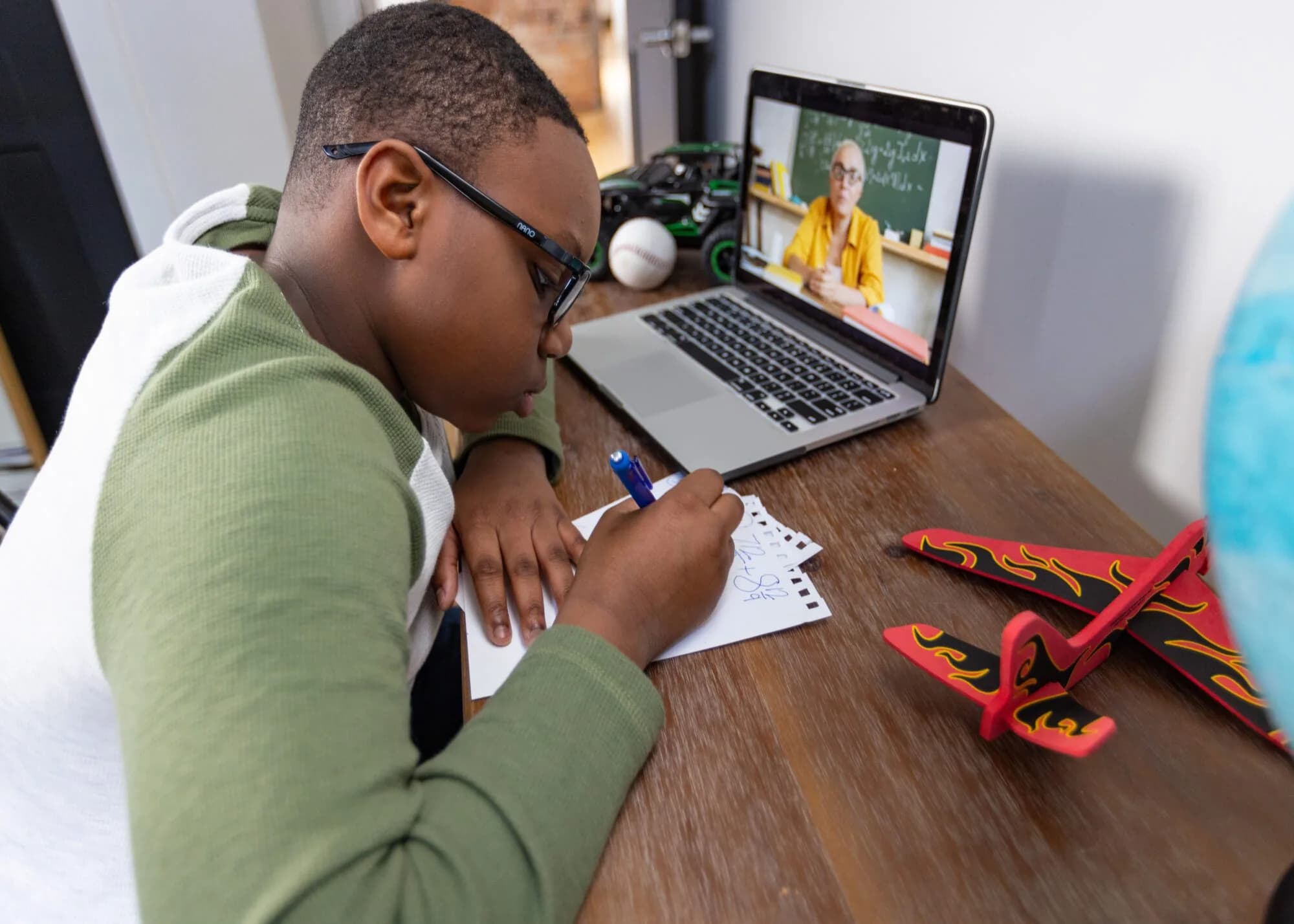 Middle school student taking notes at a desk during a live online class on a laptop