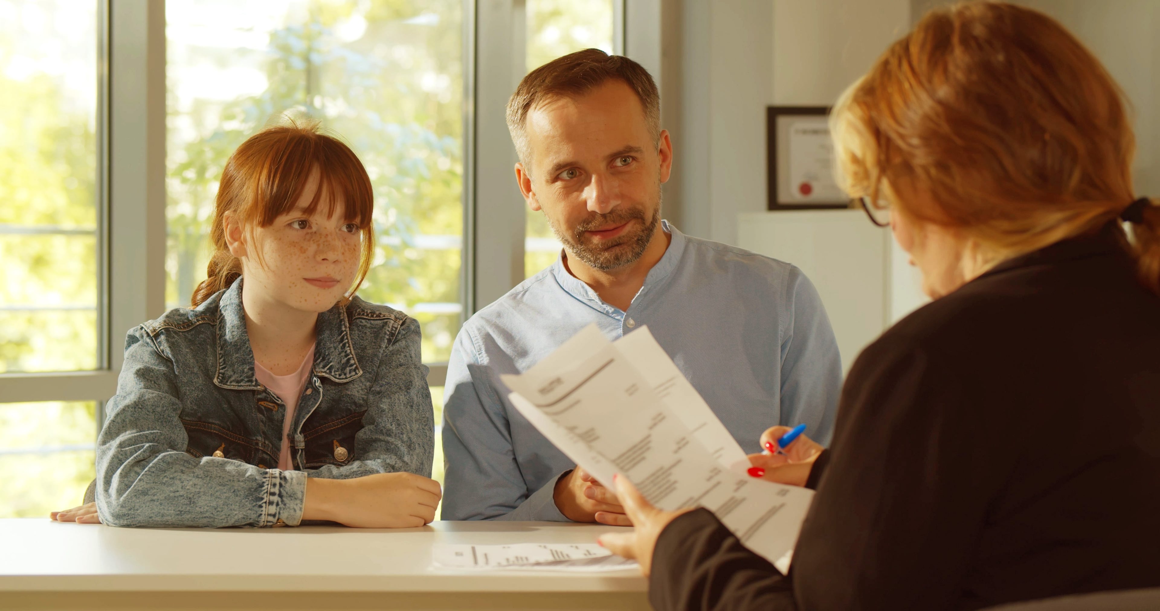 Adult and child reviewing documents with another adult at a table.