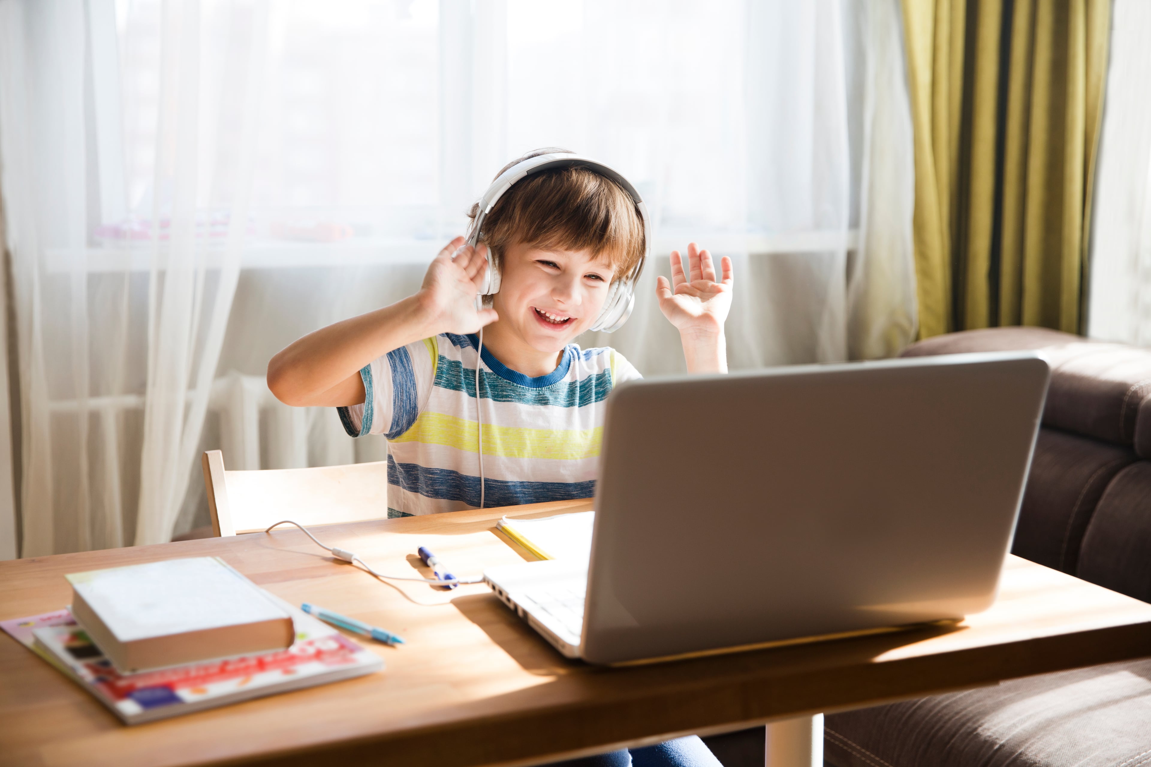 Smiling child with headphones and laptop, hands raised.